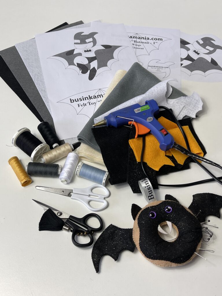 Batman felt toy sewing pattern with stiff felt, thread, scissors, glue gun and craft supplies for a handmade plushie project