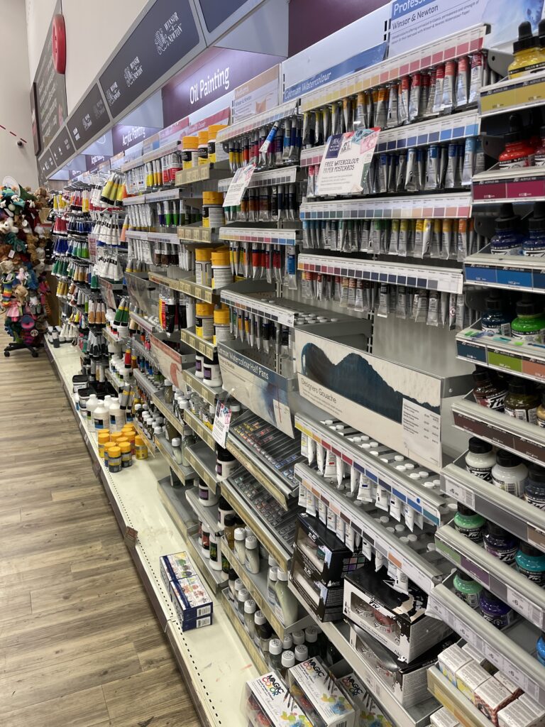 Craft shop aisle filled with fabric paint and art supplies for painting black stripes on a handmade felt tiger plushie