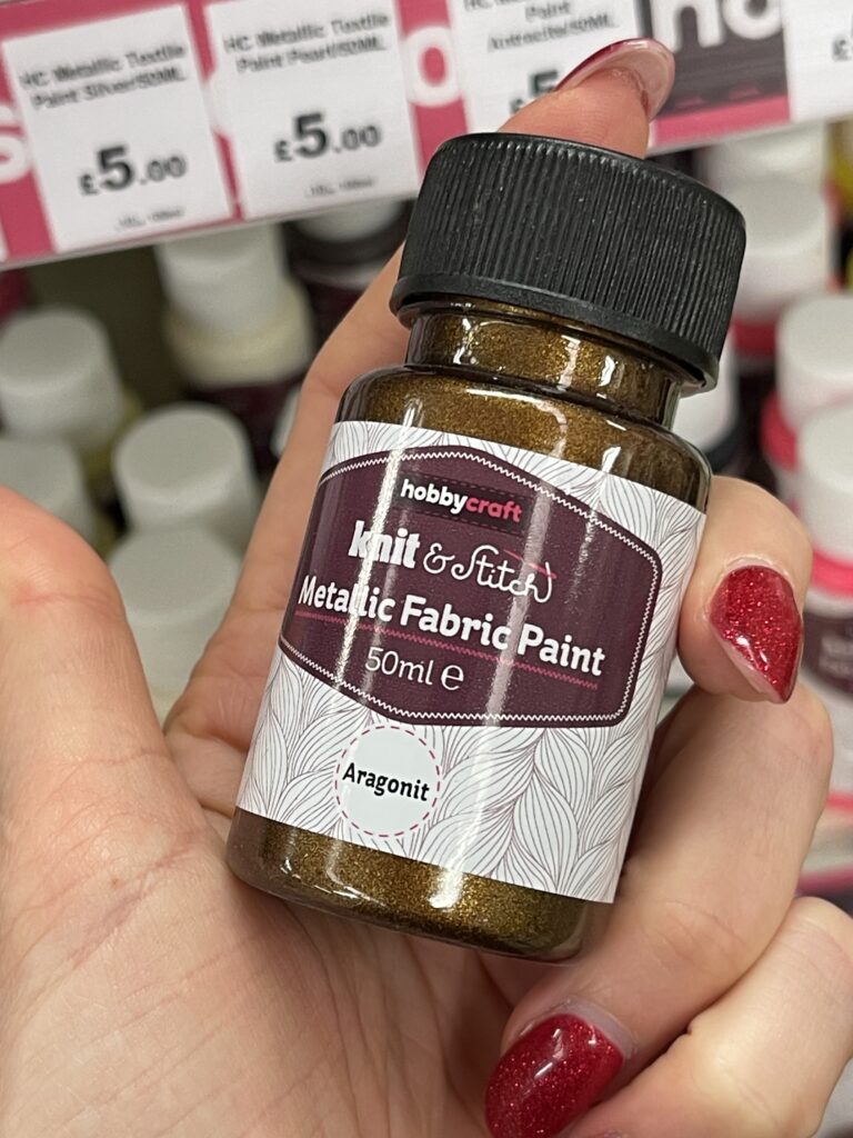 Golden metallic fabric paint held in a craft shop for adding decorative details to handmade felt toys and plushie projects