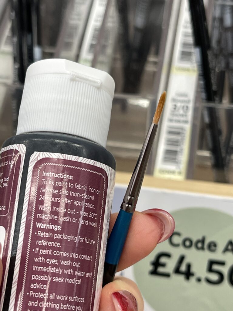 Thin paintbrush beside black fabric paint for adding precise stripes to a handmade felt tiger plushie craft project